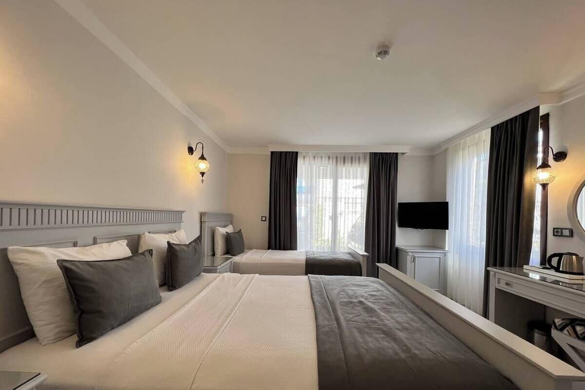 A hotel room with two beds, a desk, a TV, and a window with curtains.