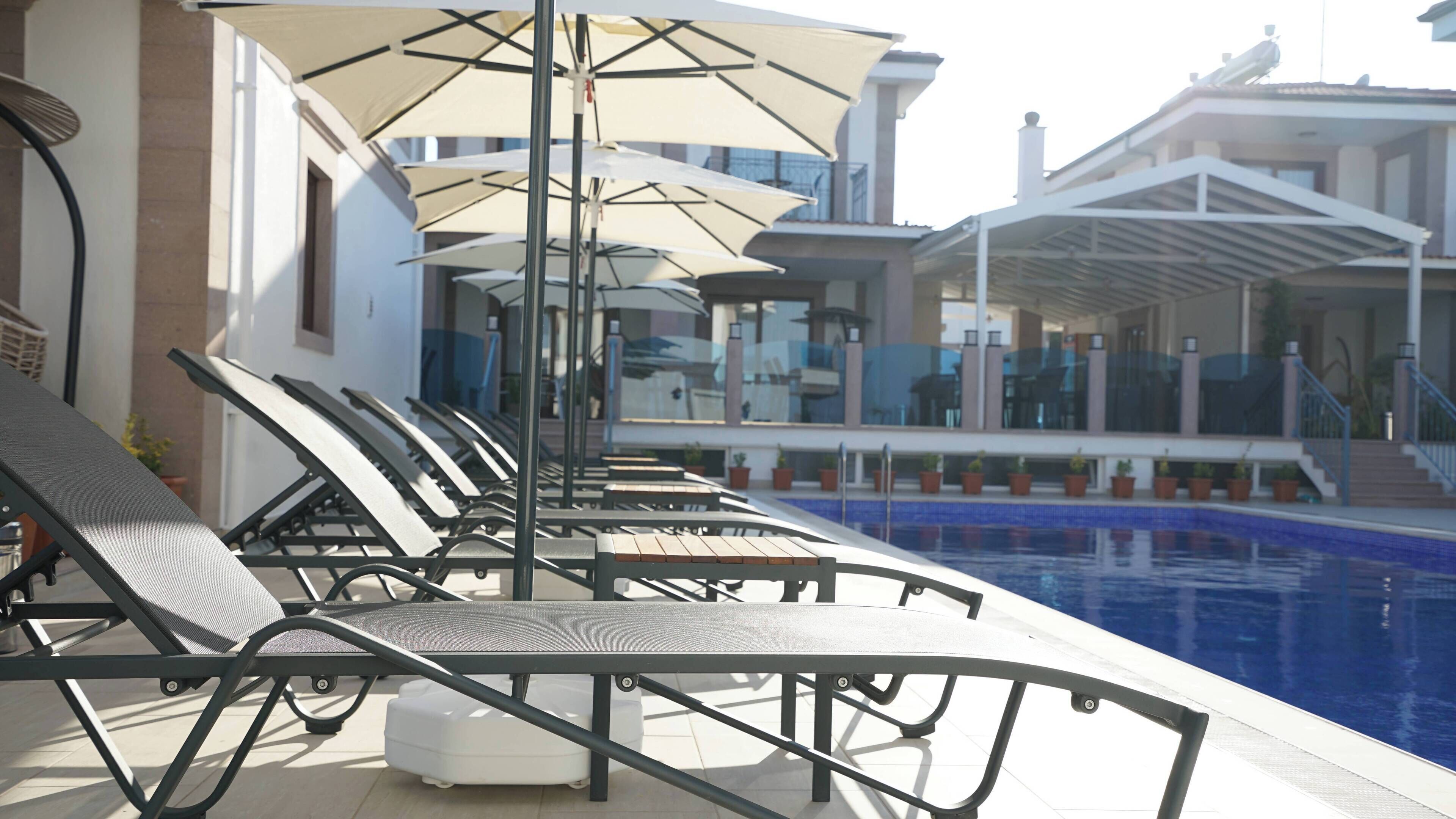 A poolside area with lounge chairs and umbrellas, a clear blue pool, and a building with a covered walkway in the background.
