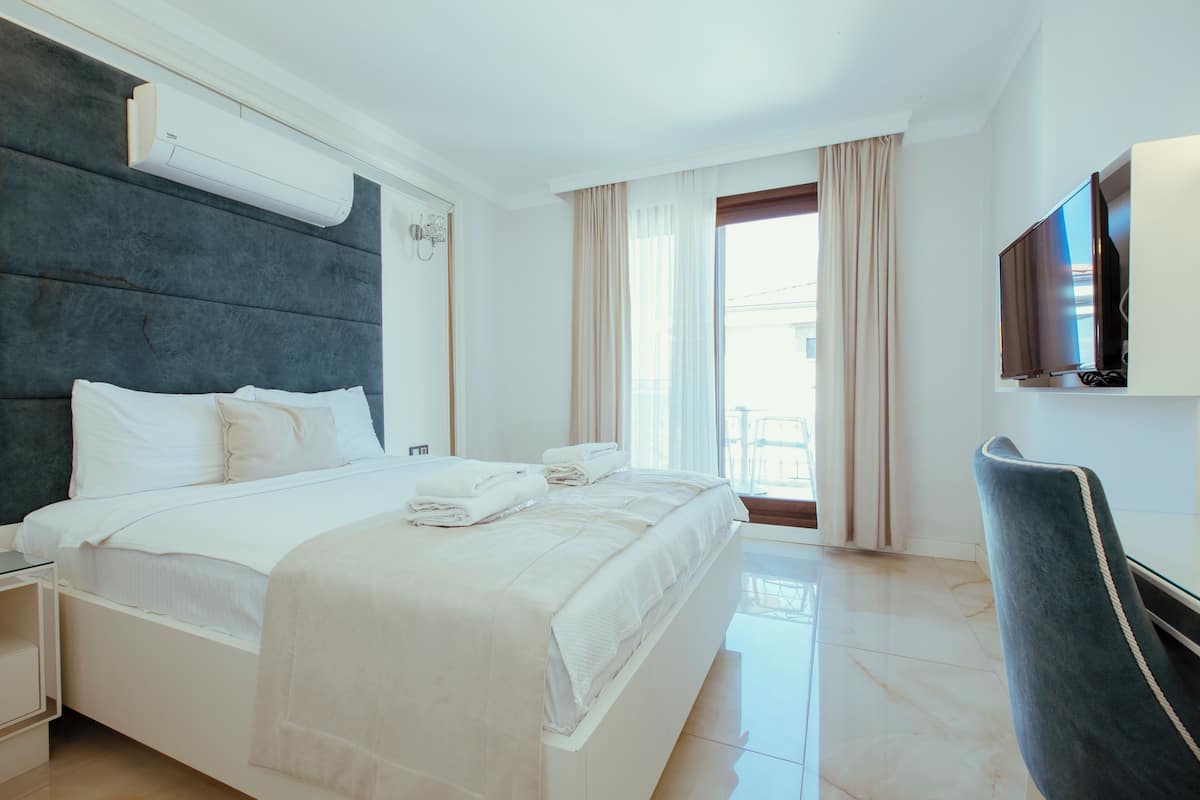 A hotel room with a large bed, a flat-screen TV, and a window with curtains.