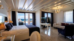 A hotel room with a bed, a sofa, a TV, and a desk. There is a view of the sea through the windows. - Cunda Say Resort (Ayvalik)