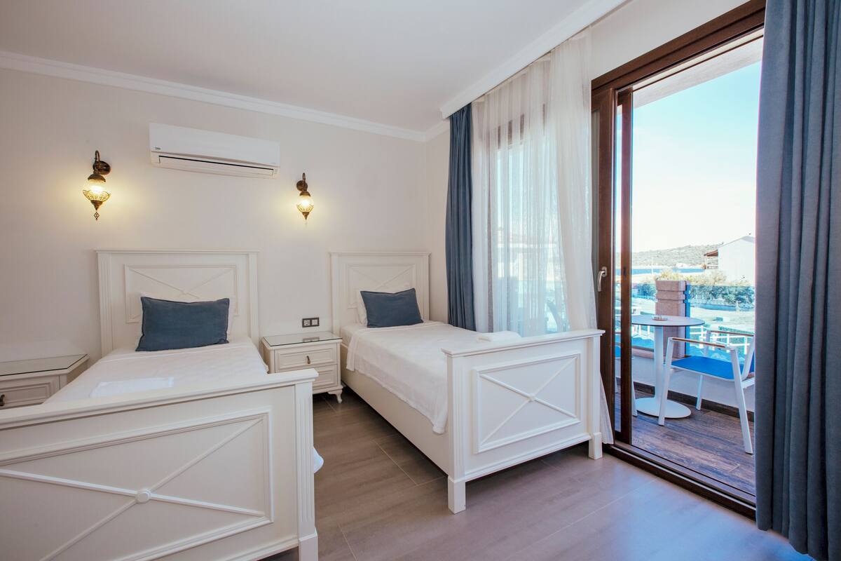 A hotel room with two beds, a balcony with a table and chairs, and an air conditioning unit.