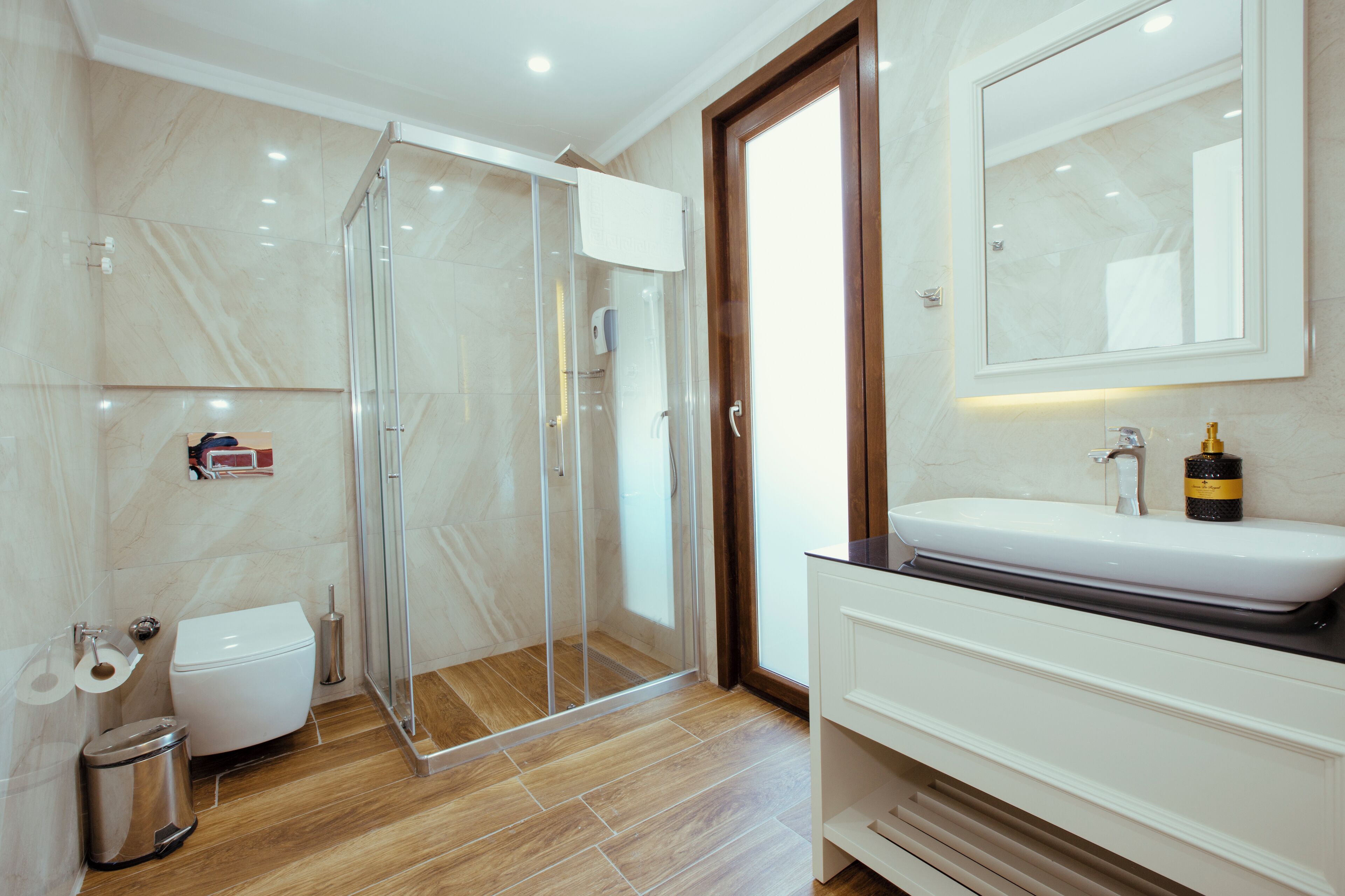 Een moderne badkamer met een douche in een glazen cabine, een wit toilet en een wastafel met een spiegel erboven.