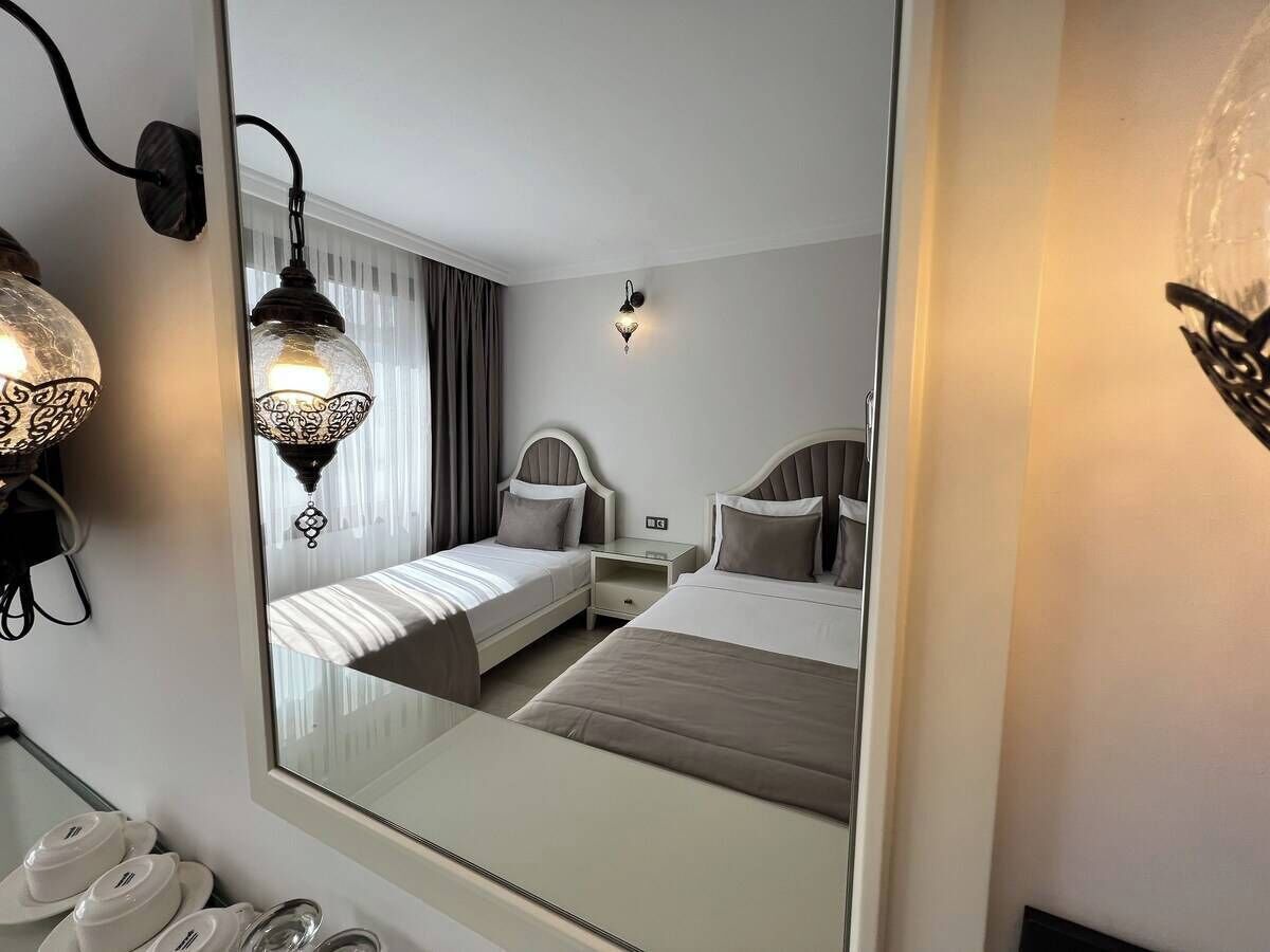 A hotel room with two beds, a nightstand, a mirror, and a wall-mounted light fixture.
