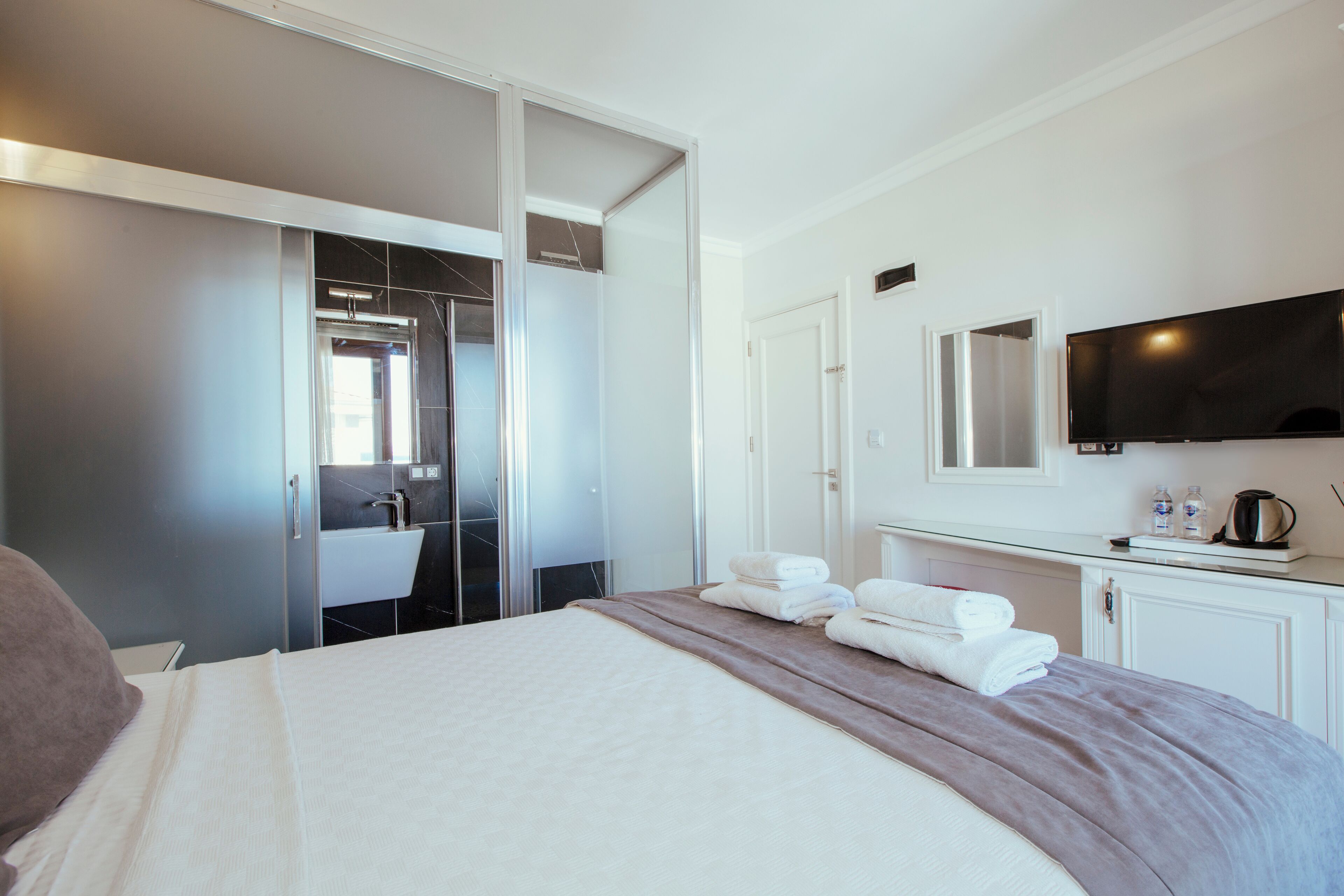 Een hotelkamer met een bed, een badkamer met een wastafel, een spiegel en een aan de muur bevestigde televisie.