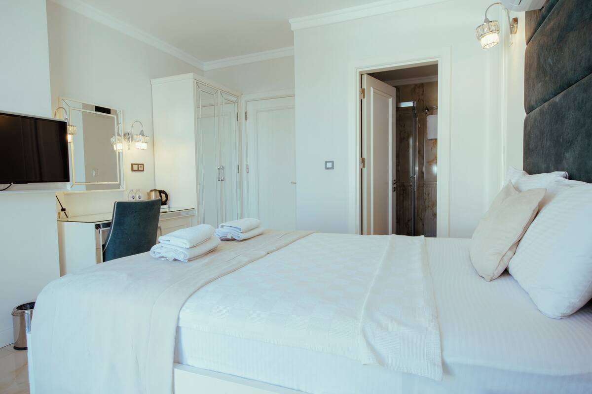 A hotel room with a large bed, a desk with a chair, a television, and a wardrobe.