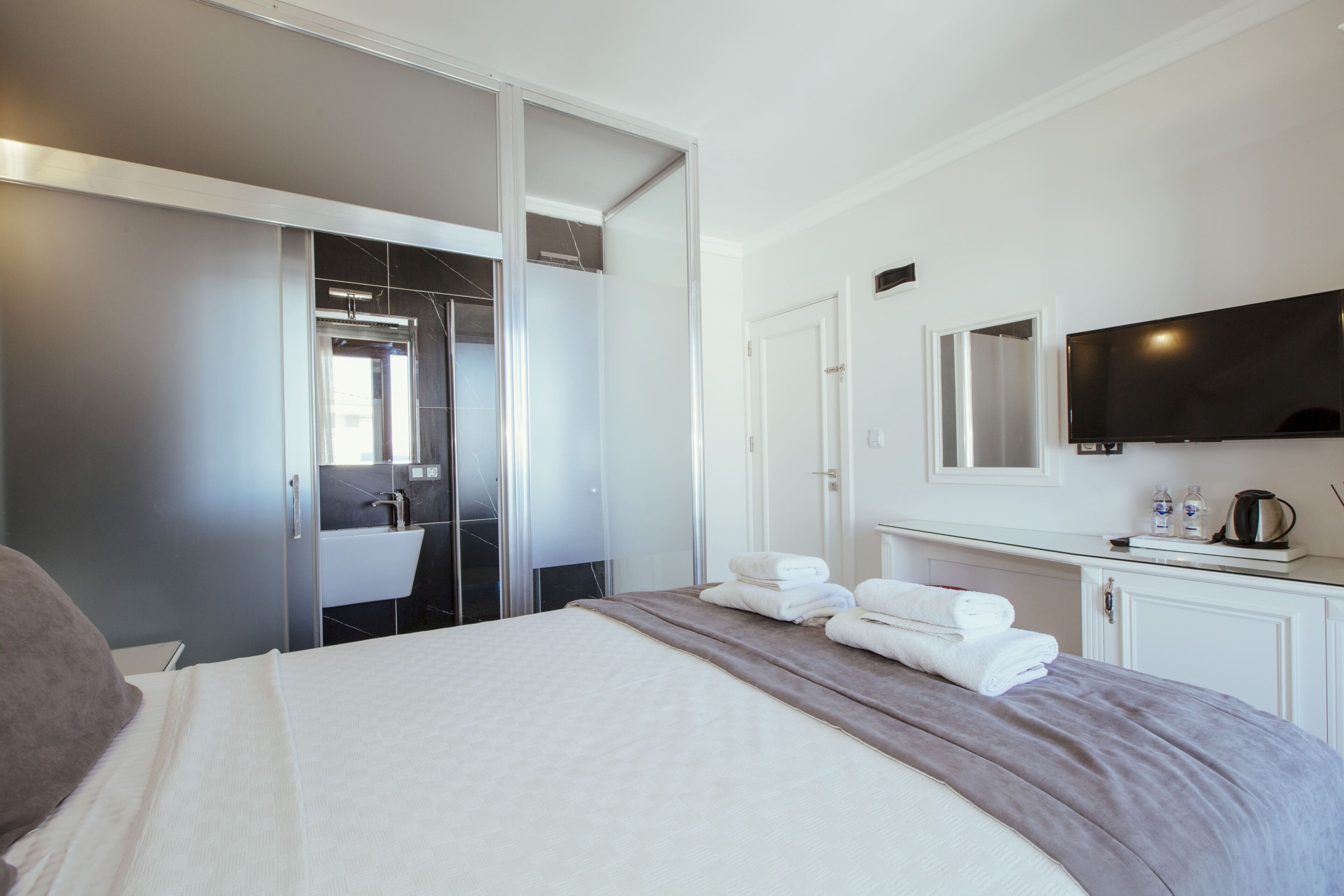 A hotel room with a bed, a TV, a bathroom with a mirror, and a cabinet.