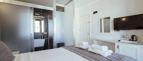 A hotel room with a bed, a TV, a bathroom with a mirror, and a cabinet.