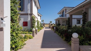 A pathway flanked by buildings with balconies, a red door, and lush greenery. - Cunda Say Resort (Ayvalik)