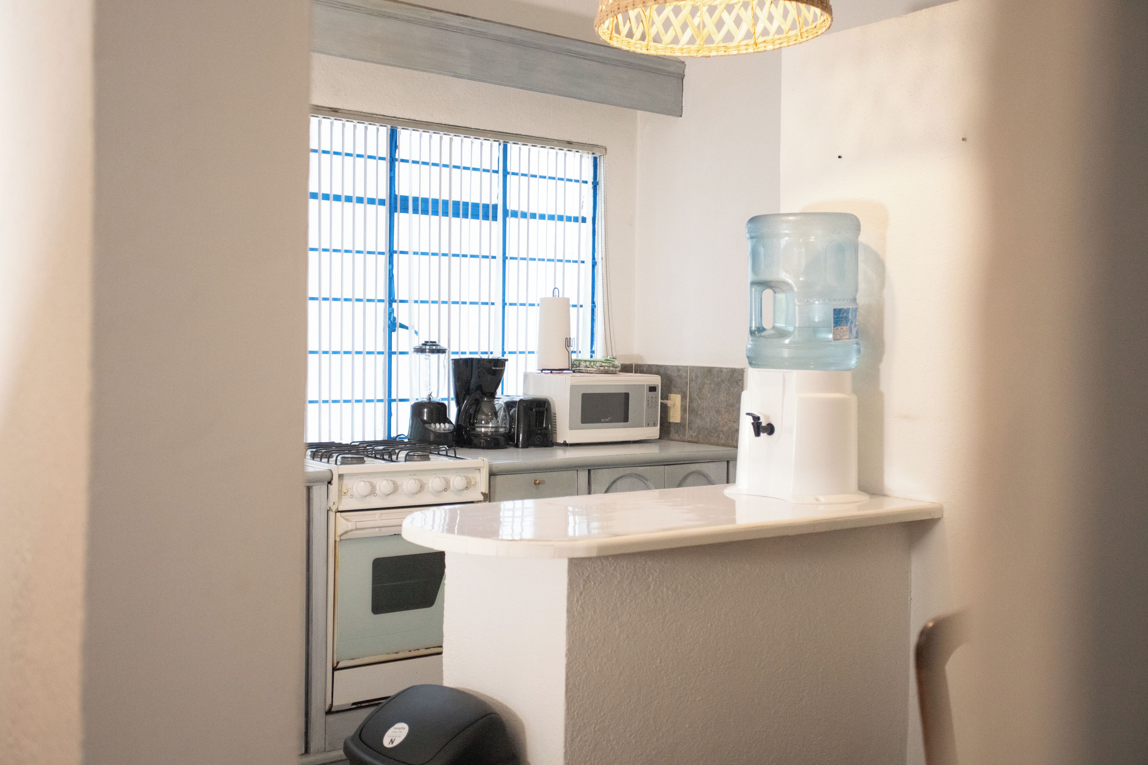 Una cocina compacta con estufa a gas, microondas, tostadora y dispensador de agua.