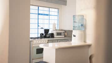 Una cocina compacta con estufa a gas, microondas, tostadora y dispensador de agua.
