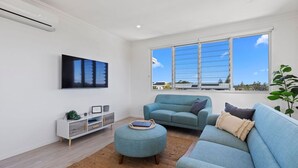 A modern living room with a large window, a flat-screen TV, a sofa, and a side table. - Boronia Beach House One - 650m to headland (Sawtell)