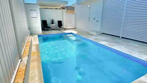 A rectangular swimming pool with a tiled deck, surrounded by a white wall and a closed shutter door. - Boronia Beach House One - 650m to headland (Sawtell)