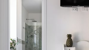 A modern bathroom with a glass shower, a white vanity, and a flat-screen TV mounted on the wall.