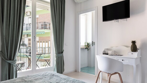 A hotel room with a bed, a desk, a chair, a TV, and a balcony with a view of a building.