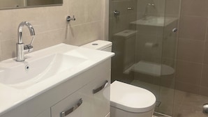 A modern bathroom with a white vanity, a glass shower enclosure, and a toilet. - Woolpack Hotel (Parramatta)