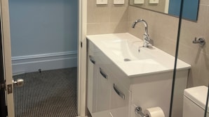 A bathroom with a white sink, a mirror, and a toilet. There are three electrical outlets on the wall. - Woolpack Hotel (Parramatta)