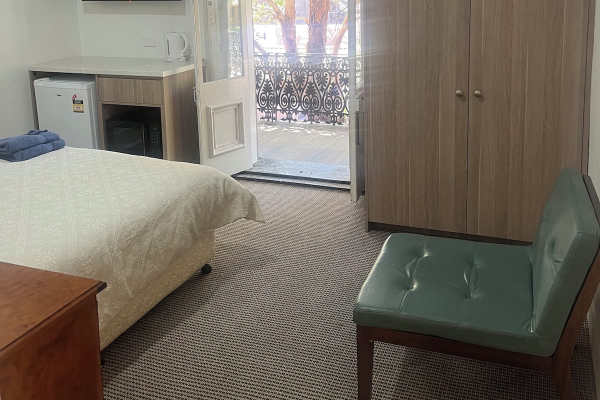 A hotel room with a bed, a desk with a computer, a television, a wardrobe, and a balcony with a view of trees.