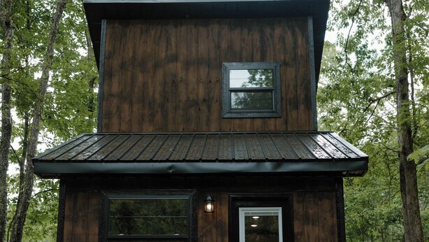 A wooden cabin with a black door, a small window, and a wooden staircase leading up to the entrance. - Cozy Tiny Home in the woods of Middle Tennessee with AC and high speed internet (Summertown)