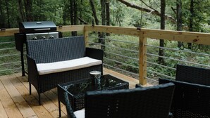 An outdoor deck with wicker furniture, a grill, and a view of a forest. - Cozy Tiny Home in the woods of Middle Tennessee with AC and high speed internet (Summertown)