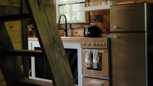 A kitchen with wooden walls, a stainless steel refrigerator, an oven, and a window above the sink. - Cozy Tiny Home in the woods of Middle Tennessee with AC and high speed internet (Summertown)