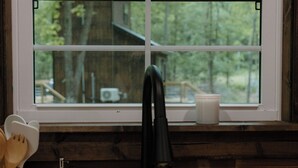 A kitchen with a stainless steel sink, wooden countertop, and a window with a view of trees. - Cozy Tiny Home in the woods of Middle Tennessee with AC and high speed internet (Summertown)