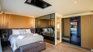 A modern bedroom with a large bed, a bedside table, a bench, and a glass partition.