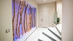 A hallway with a modern art installation of twisted branches, a door, and a staircase leading to a seating area with a plant.