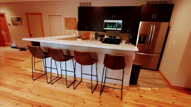 Eine moderne Küche mit einer zentralen Kochinsel, vier Barhocker, Edelstahlgeräten und Holzböden.