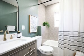 Bathroom features a white sink, toilet, and bathtub, with a striped shower curtain and a framed artwork on the wall.