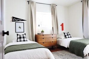 Two single beds with green throw blankets, a dresser, and a potted plant create a cozy atmosphere.