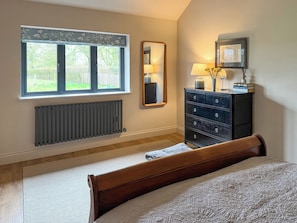 A bedroom with a bed, a dresser, a mirror, a radiator, and a window with a view of greenery. - 1 bedroom accommodation in Eye (Eye)