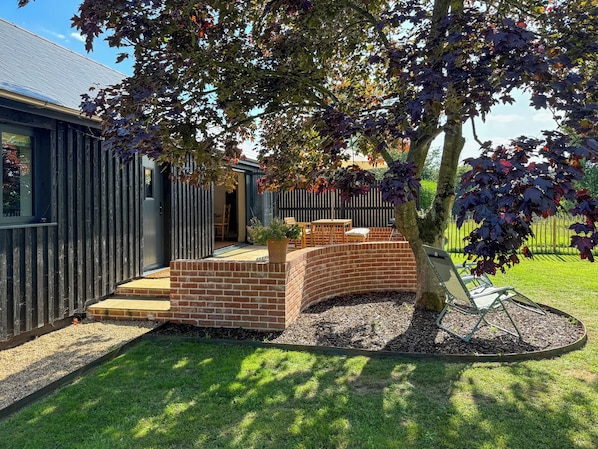 A modern house with a brick patio, a wooden fence, and a tree in the yard.