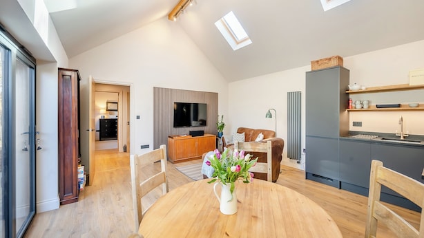 A modern loft-style living space with a dining area, kitchen, and a TV mounted on the wall. - 1 bedroom accommodation in Eye (Eye)
