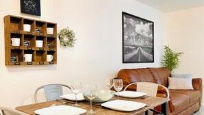 Un comedor con mesa de madera dispuesta para cuatro personas, sofá de cuero marrón y barra de café montada en la pared.