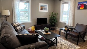 Una sala de estar con sofá, sillón, mesa de centro, televisor y una planta en maceta.