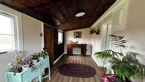 Una habitación con suelo de madera, un escritorio, un atril de mimbre y una planta grande en maceta.