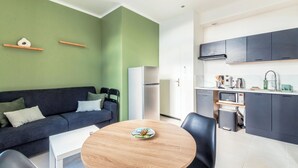 A modern living space with a dark blue sofa, a round wooden table, and a kitchen area with dark cabinets and a microwave. - Cosy, quiet, air-conditioned T2 apartment (Villeurbanne)