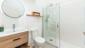 A modern bathroom with a white sink, a toilet, a glass shower enclosure, and a round mirror. - Cosy, quiet, air-conditioned T2 apartment (Villeurbanne)