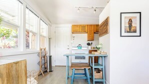 A kitchen with wooden cabinets, a blue table, and a window overlooking greenery.