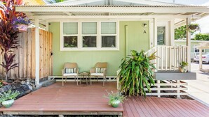 A covered porch with two wicker chairs and a small table, a green wall, and a wooden fence.