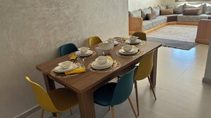 Un tavolo da pranzo apparecchiato con piatti, ciotole e bicchieri bianchi, circondato da sedie gialle e blu.