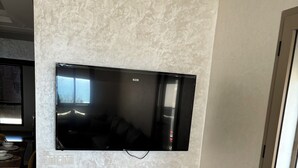 Un soggiorno moderno con una TV a schermo piatto montata su una parete strutturata, mensole in legno sottostanti e un'area pranzo visibile sullo sfondo.