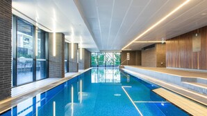 Une piscine intérieure moderne, avec une eau d’un bleu limpide, de grandes fenêtres et une vue sur la verdure environnante.