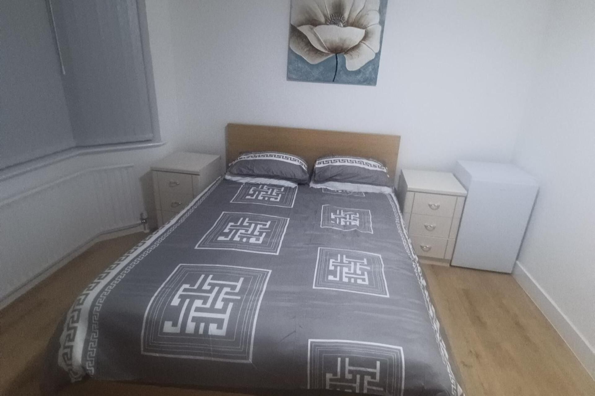 A bedroom with a bed, two bedside tables, a nightstand, and a wall-mounted artwork.