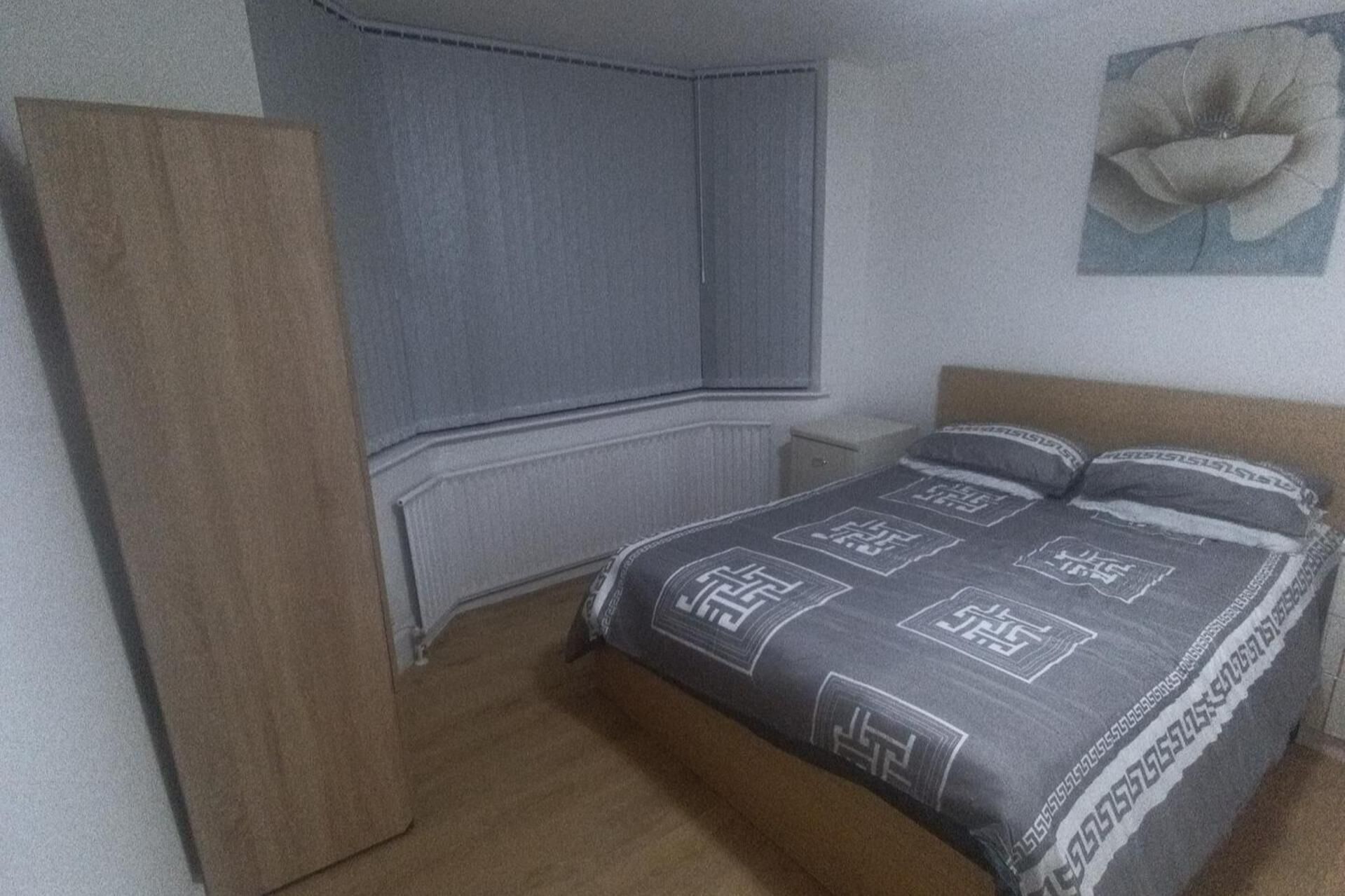 A bedroom with a bed, a nightstand, a dresser, and a wall-mounted radiator.