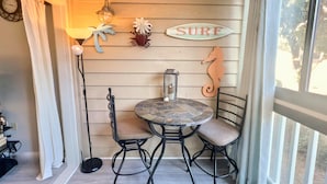 A cozy corner with a round stone table and two chairs, a 'SURF' sign, a lantern, and a seahorse decoration on a wooden wall. - BEAUTY on The Sound!  Port Royal Hilton Head, Gorgeous, Peaceful Sleeps 6/2br2ba (Hilton Head)