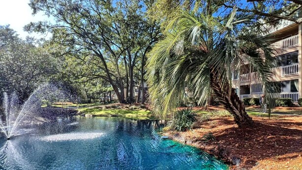A clear blue pool with a water fountain, surrounded by trees and a building with balconies. - BEAUTY on The Sound!  Port Royal Hilton Head, Gorgeous, Peaceful Sleeps 6/2br2ba (Hilton Head)