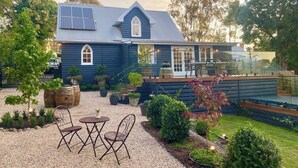 Une maison bleue dotée de panneaux solaires, une terrasse avec des chaises et un jardin où poussent différentes plantes ainsi qu’un petit arbre.