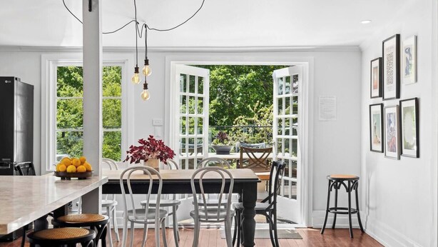 Une cuisine moderne avec une table en bois, des chaises blanches et un luminaire suspendu.
