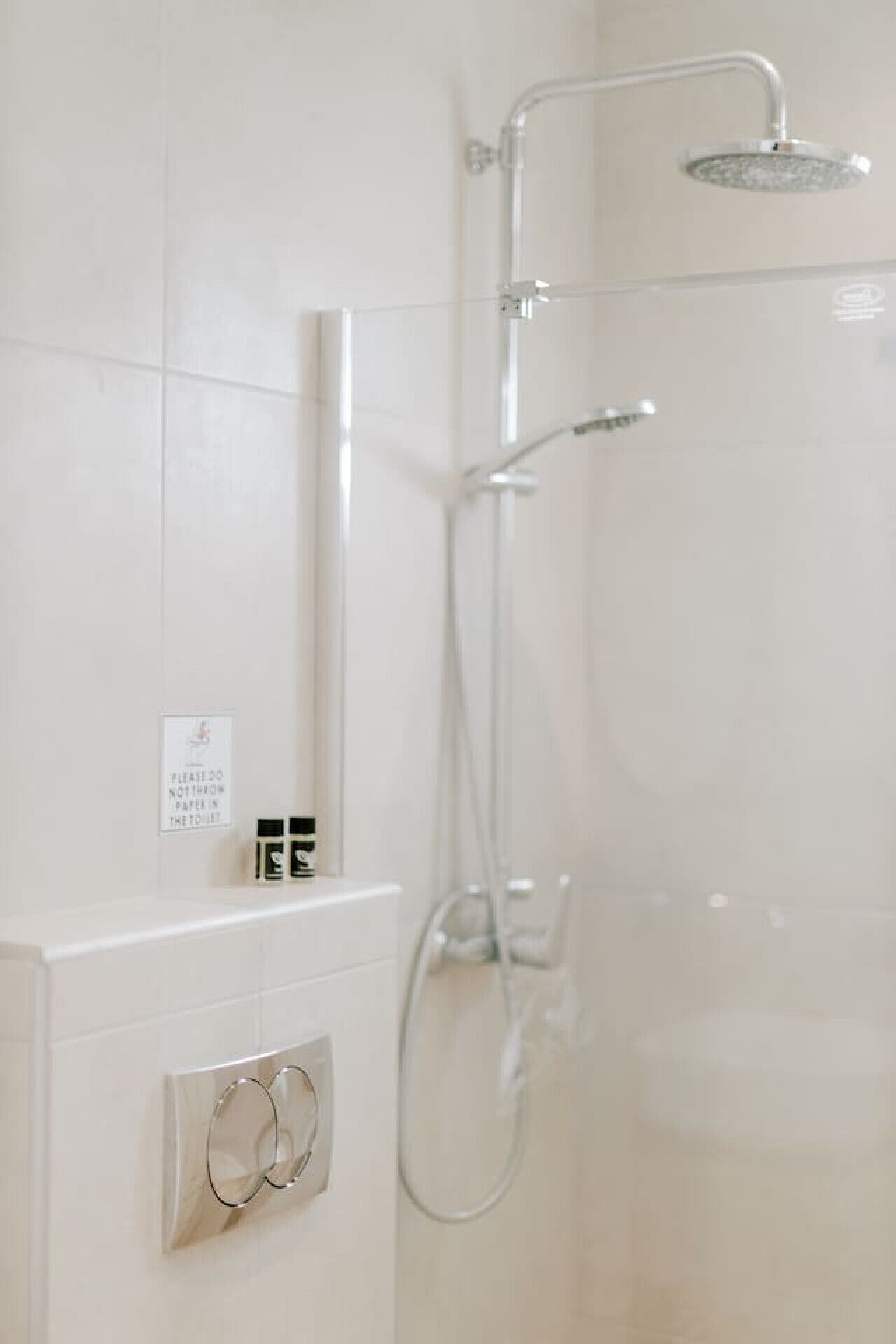 Et moderne badeværelse med en brusekabine i glas, toiletpapirholder og et panel til betjening på væggen.